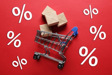 Image of Hot sale, special offer. Percent signs around shopping cart and boxes on red background, top view