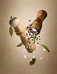 Image of Salt and pepper mills, bay leaves, coarse salt and peppercorns flying against beige gradient background