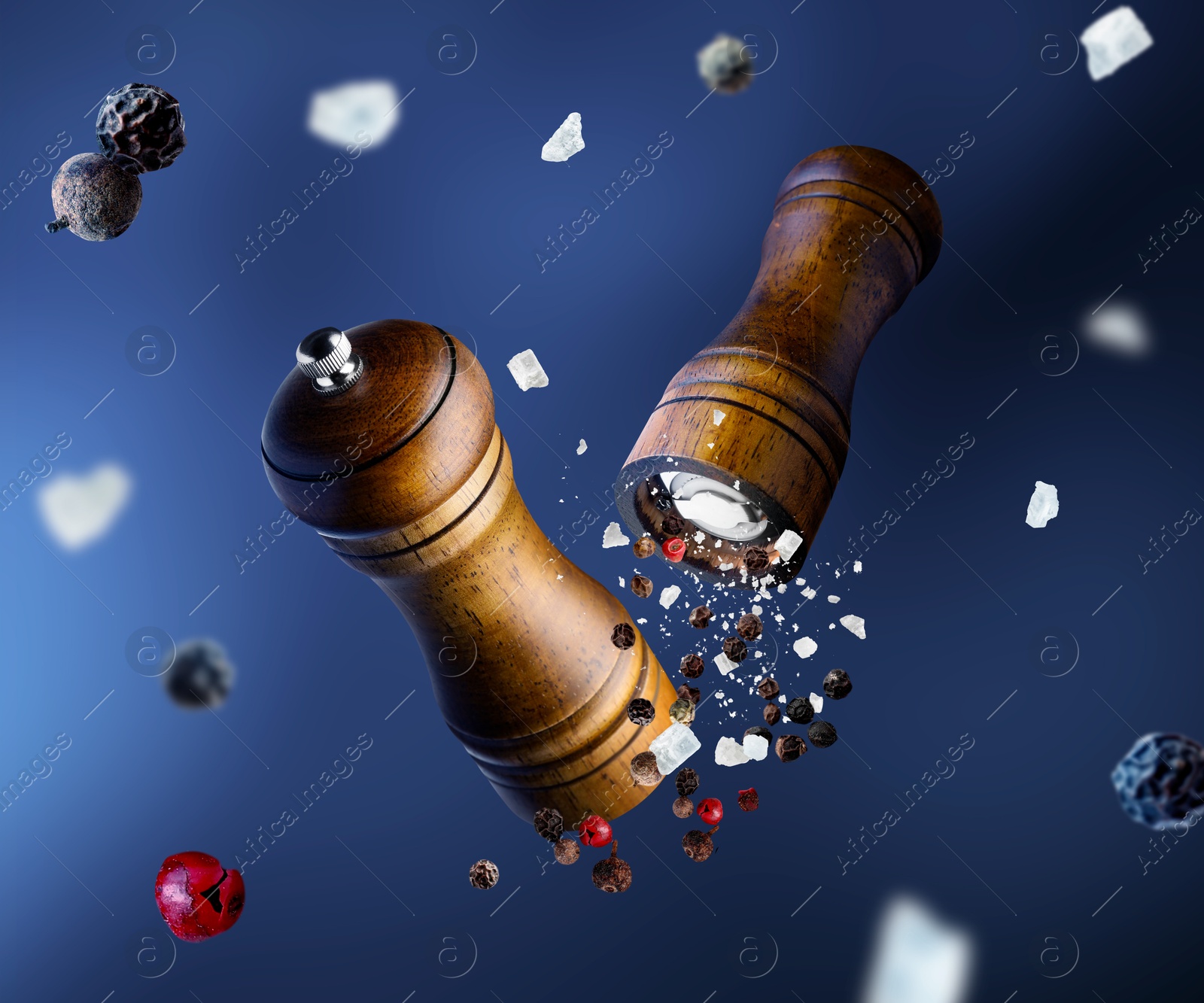 Image of Salt and pepper mills, coarse salt and peppercorns flying against blue gradient background
