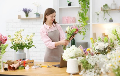 Photo of Professional florist making bouquet of flowers at wooden table in shop