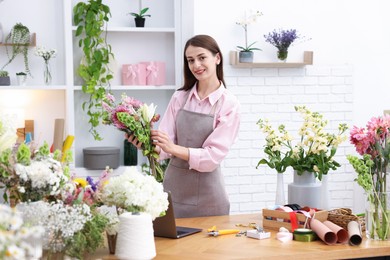Photo of Professional florist making bouquet of flowers at wooden table in shop