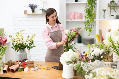 Photo of Professional florist making bouquet of flowers at wooden table in shop