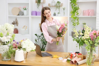 Photo of Professional florist making bouquet of flowers at wooden table in shop