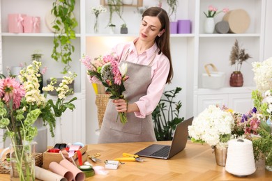 Photo of Professional florist making bouquet of flowers at wooden table in shop