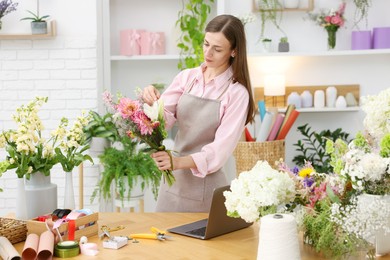 Photo of Professional florist making bouquet of flowers at wooden table in shop