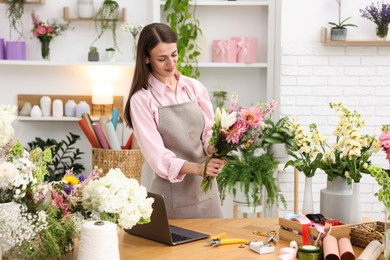 Photo of Professional florist making bouquet of flowers at wooden table in shop