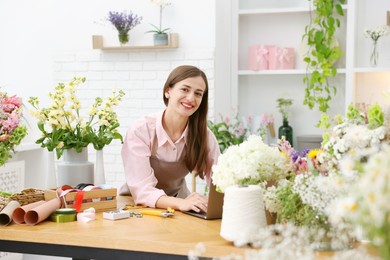 Photo of Professional florist working with laptop at wooden table in shop