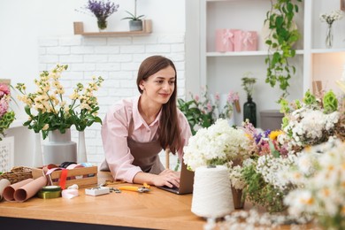 Photo of Professional florist working with laptop at wooden table in shop