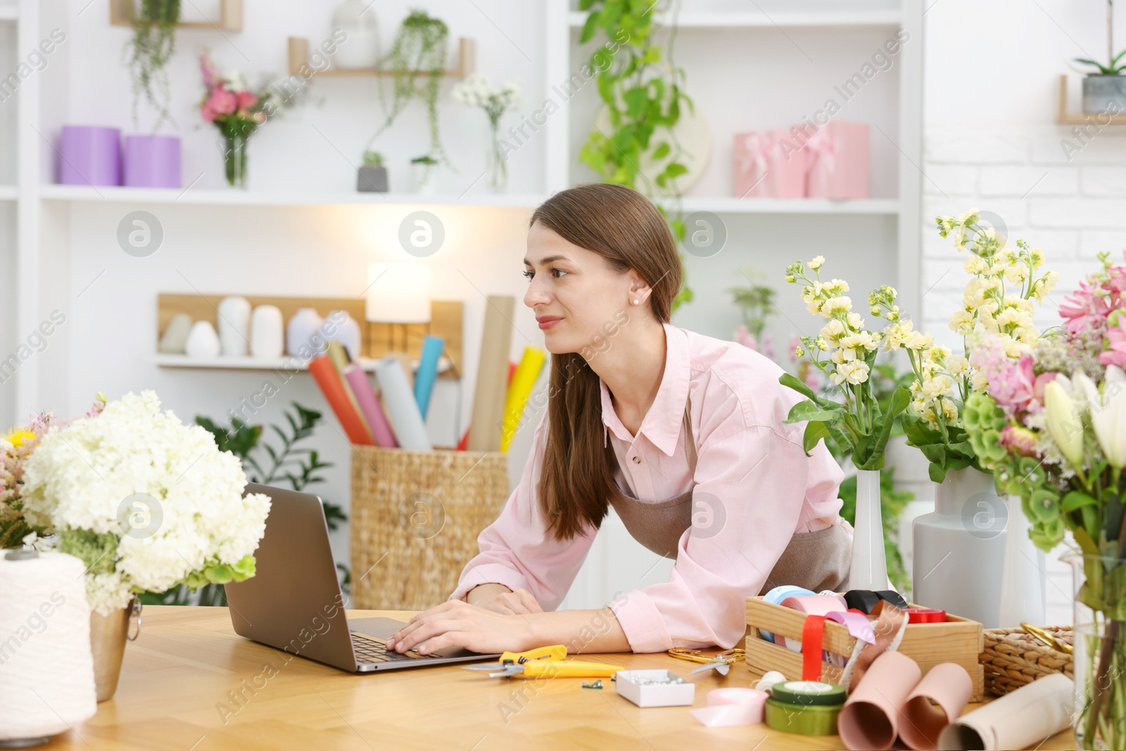 Professional florist working with laptop at wooden table in shop Photo of Professional florist working with laptop at wooden table in shop