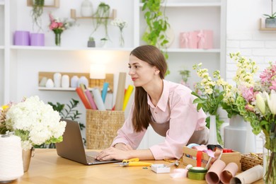 Photo of Professional florist working with laptop at wooden table in shop