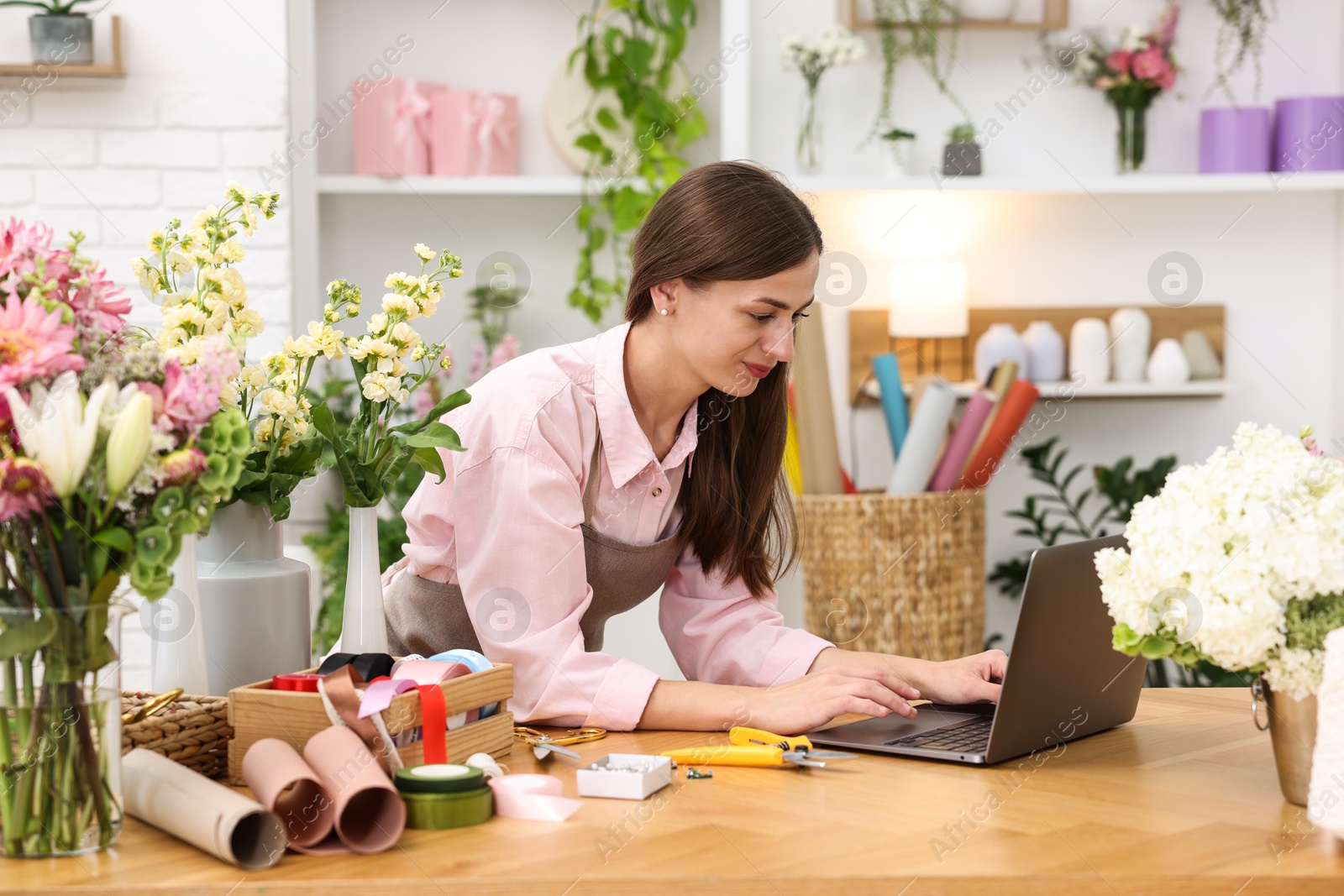 Professional florist working with laptop at wooden table in shop Photo of Professional florist working with laptop at wooden table in shop