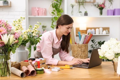 Photo of Professional florist working with laptop at wooden table in shop
