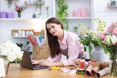 Photo of Professional florist working with laptop at wooden table in shop