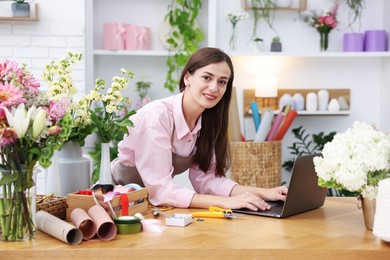Photo of Professional florist working with laptop at wooden table in shop