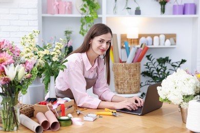Photo of Professional florist working with laptop at wooden table in shop