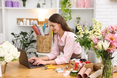 Photo of Professional florist working with laptop at wooden table in shop