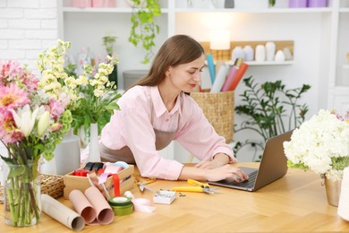 Photo of Professional florist working with laptop at wooden table in shop
