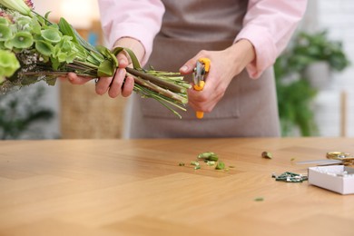 Photo of Professional florist making bouquet of flowers at wooden table in shop, closeup