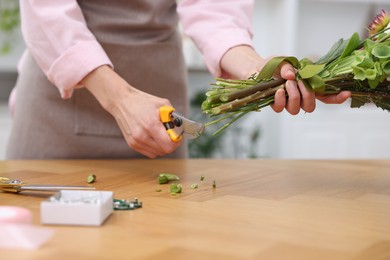 Photo of Professional florist making bouquet of flowers at wooden table in shop, closeup