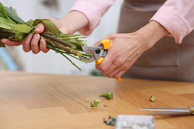 Photo of Professional florist making bouquet of flowers at wooden table in shop, closeup