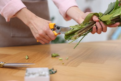 Photo of Professional florist making bouquet of flowers at wooden table in shop, closeup