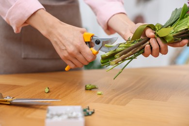 Photo of Professional florist making bouquet of flowers at wooden table in shop, closeup
