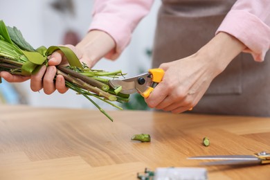 Photo of Professional florist making bouquet of flowers at wooden table in shop, closeup