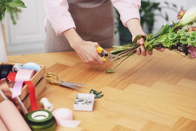 Photo of Professional florist making bouquet of flowers at wooden table in shop, closeup