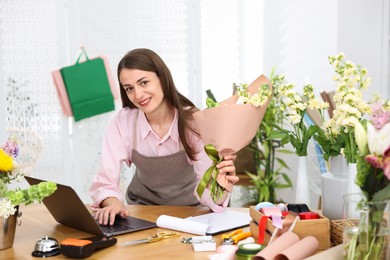 Photo of Professional florist working with laptop at wooden table in shop