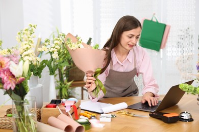 Photo of Professional florist working with laptop at wooden table in shop