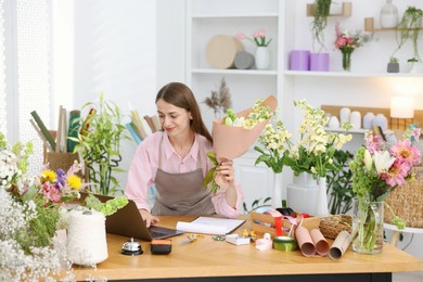 Photo of Professional florist working with laptop at wooden table in shop