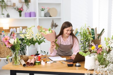 Photo of Professional florist working with laptop at wooden table in shop