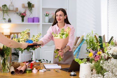Photo of Florist with bouquet of flowers taking payment from client via terminal in shop