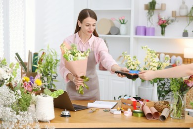 Photo of Florist with bouquet of flowers taking payment from client via terminal in shop