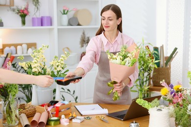 Photo of Florist with bouquet of flowers taking payment from client via terminal in shop