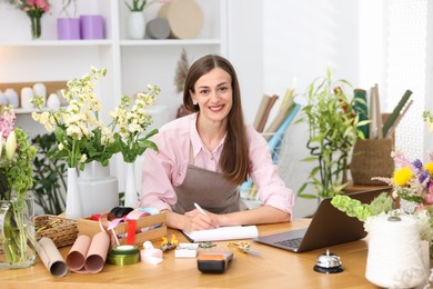 Photo of Professional florist working with laptop at wooden table in shop