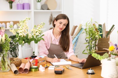 Photo of Professional florist working with laptop at wooden table in shop