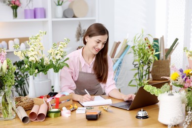 Photo of Professional florist working with laptop at wooden table in shop