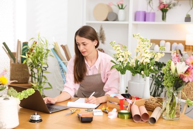 Photo of Professional florist working with laptop at wooden table in shop