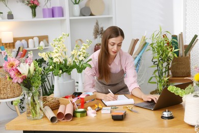 Photo of Professional florist working with laptop at wooden table in shop