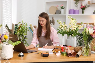 Photo of Professional florist working with laptop at wooden table in shop