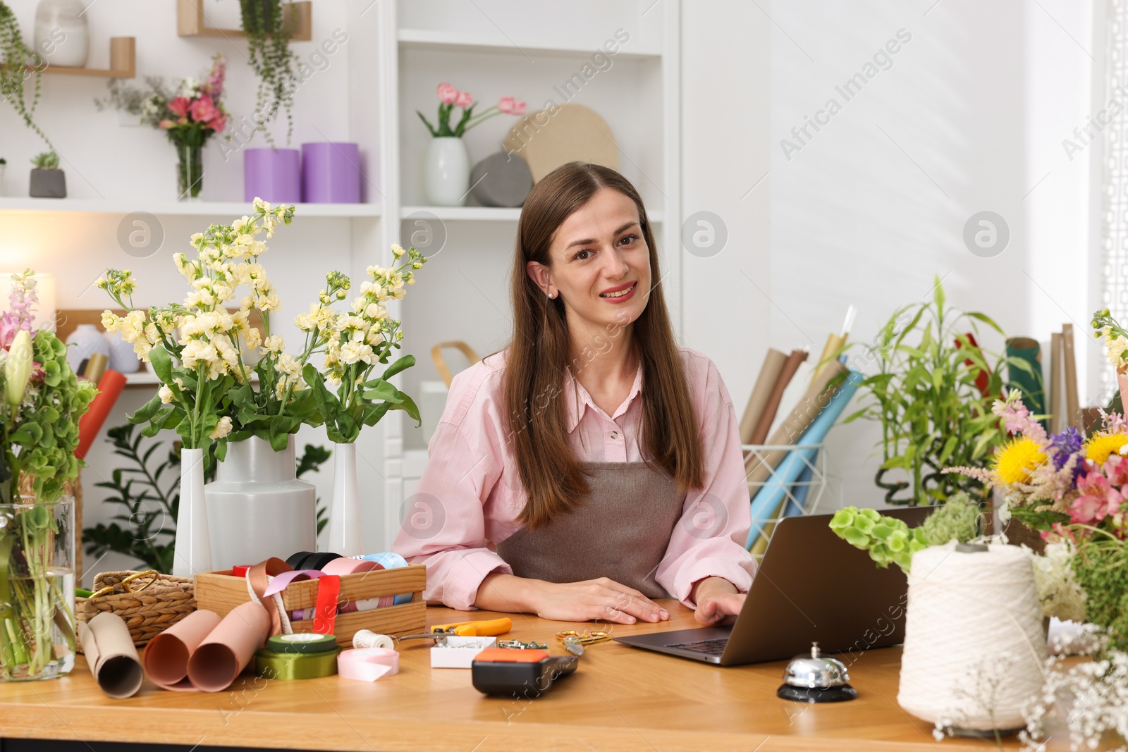 Photo of Professional florist working with laptop at wooden table in shop