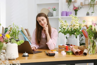 Photo of Professional florist working with laptop at wooden table in shop