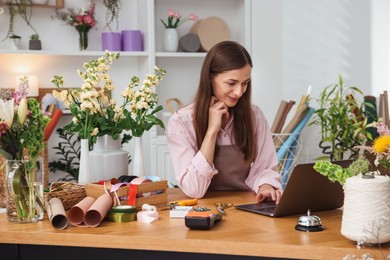 Photo of Professional florist working with laptop at wooden table in shop