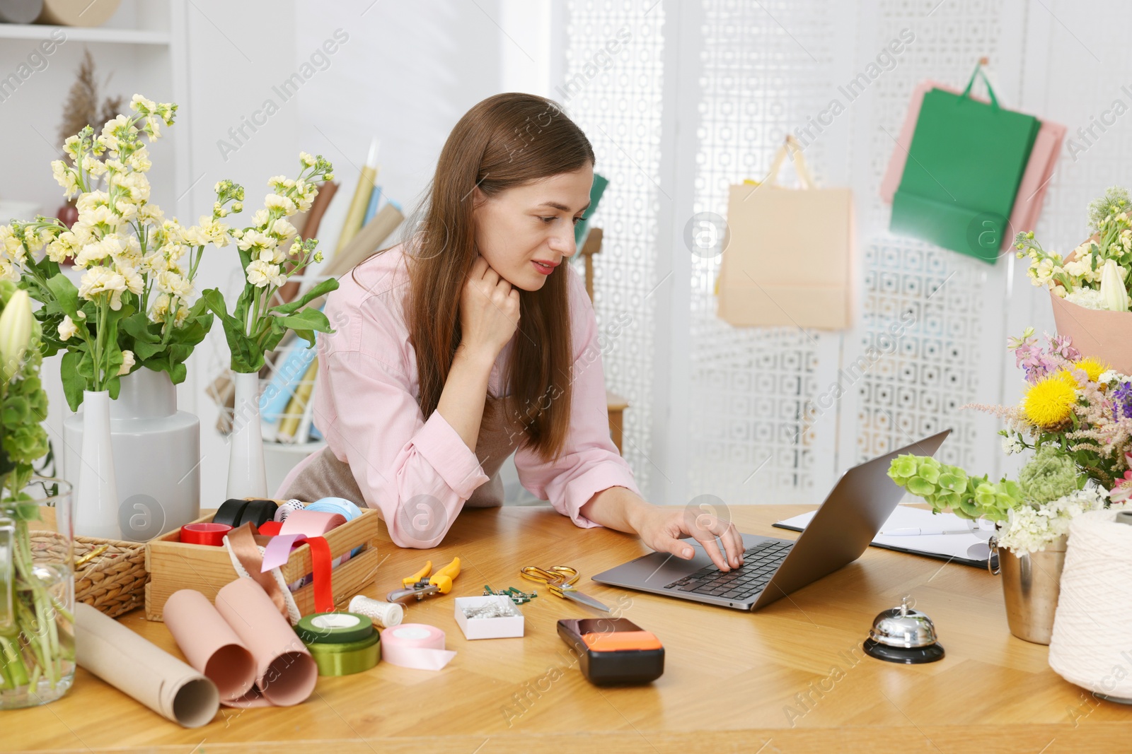 Professional florist working with laptop at wooden table in shop Photo of Professional florist working with laptop at wooden table in shop