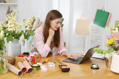 Photo of Professional florist working with laptop at wooden table in shop
