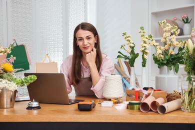 Photo of Professional florist working with laptop at wooden table in shop