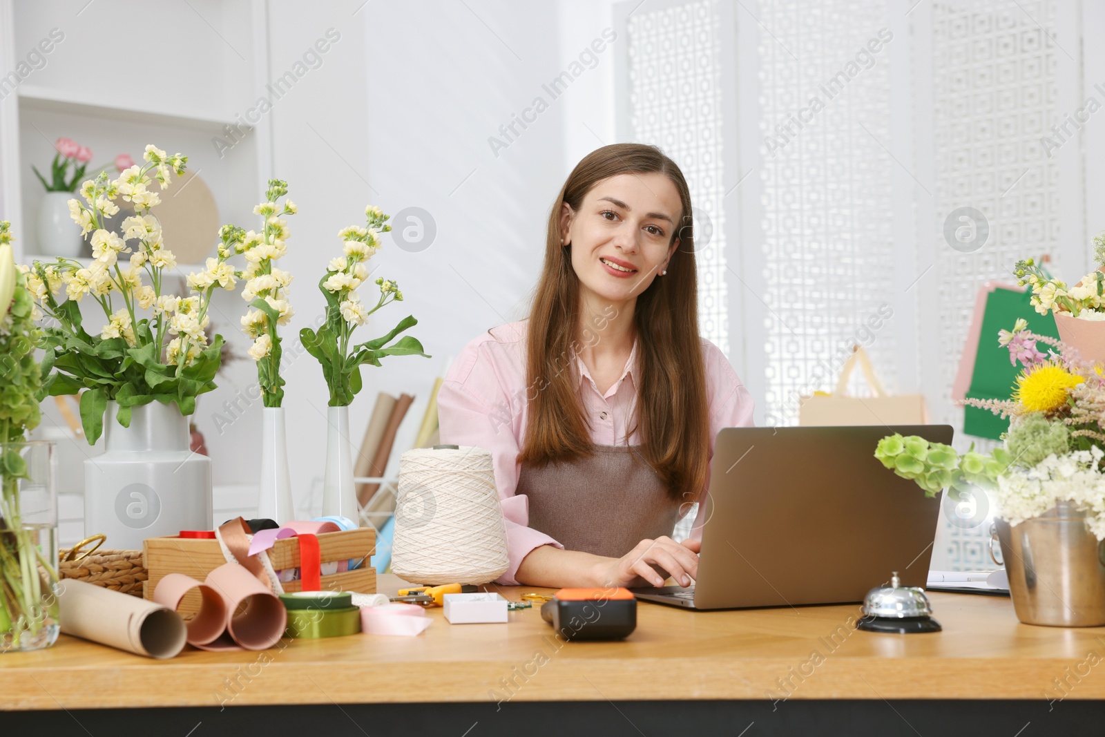Professional florist working with laptop at wooden table in shop Photo of Professional florist working with laptop at wooden table in shop
