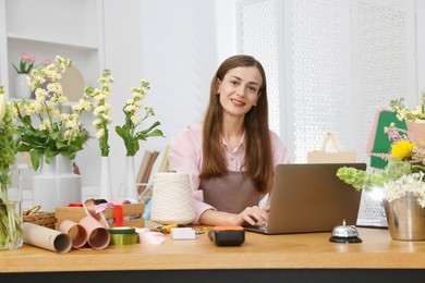 Photo of Professional florist working with laptop at wooden table in shop