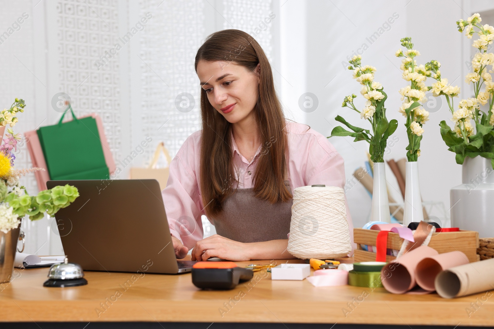 Professional florist working with laptop at wooden table in shop Photo of Professional florist working with laptop at wooden table in shop